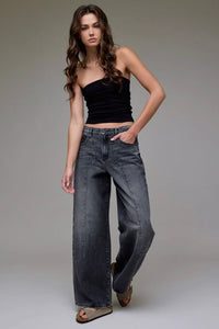 Woman wearing a black top and blue jeans against a gray background