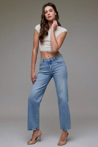 Woman wearing a white crop top and light blue jeans against a gray background