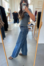 Load image into Gallery viewer, Person taking a mirror selfie wearing a gray t-shirt and blue jeans in a clothing store.