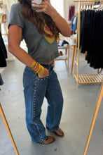 Load image into Gallery viewer, Person taking a mirror selfie wearing a graphic t-shirt and blue jeans in a clothing store.
