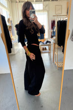 Load image into Gallery viewer, Person wearing a black outfit in a fitting room.
