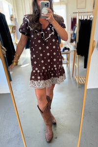 Person wearing a brown polka dot dress with lace trim and brown cowboy boots, standing in front of a mirror.
