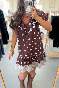 Woman wearing a brown dress with white patterns in a clothing store.