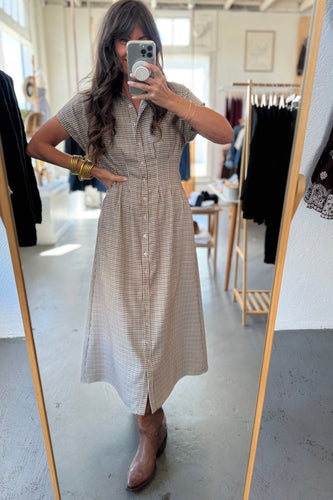 Woman taking a mirror selfie wearing a checkered dress in a clothing store.