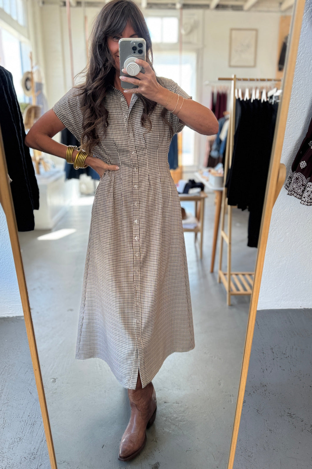 Woman taking a mirror selfie wearing a checkered dress in a clothing store.