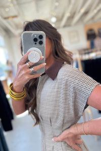Person taking a mirror selfie wearing a checkered dress in an indoor setting.