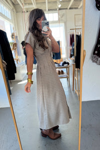 Woman taking a mirror selfie wearing a long patterned dress in a clothing store.