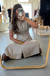 Woman taking a mirror selfie wearing a checkered dress in a clothing store.