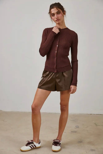 Woman wearing a brown ribbed sweater and shiny shorts with white sneakers on a plain background
