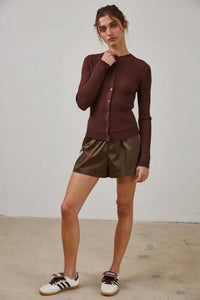 Woman wearing a brown ribbed sweater and shiny shorts with white sneakers on a plain background
