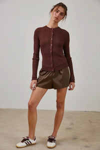 Woman wearing a brown ribbed sweater and gold shorts against a plain background