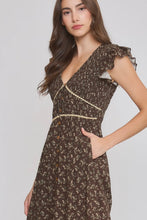 Load image into Gallery viewer, A woman wearing a dark brown floral print dress with ruffled cap sleeves, a V-neckline, and decorative beige trim details, posed against a light gray studio background.