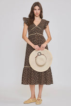 Load image into Gallery viewer, A woman modeling a brown floral midi dress with ruffled cap sleeves and a V-neckline, holding a large beige straw hat against a light gray studio background.