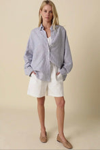 Load image into Gallery viewer, Woman wearing a light blue button-up shirt and white shorts on a beige background