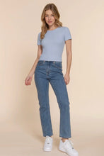 Load image into Gallery viewer, Woman wearing a light blue t-shirt and jeans on a beige background