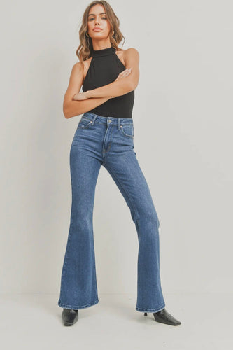 Woman wearing blue flared jeans and a black top on a plain background
