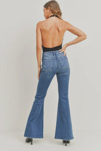 Person wearing blue flared jeans and a black top on a plain background
