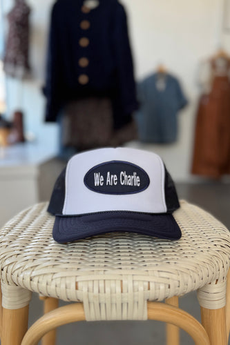 Trucker hat with 'We Are Charlie' on a wicker stool in a store setting