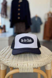 Trucker hat with 'We Are Charlie' on a wicker stool in a store setting
