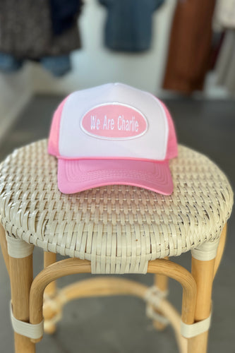 Pink and white cap with 'We Are Charlie' text on a wicker stool.