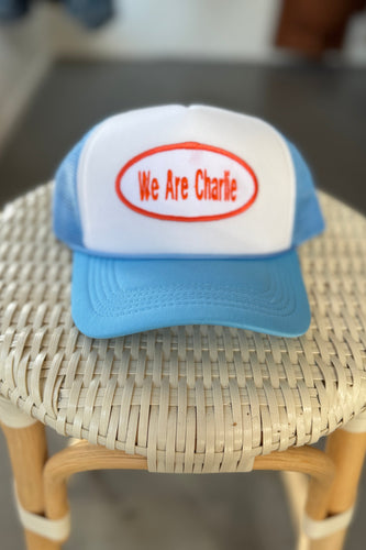 Blue and white cap with 'We Are Charlie' text on a woven stool.