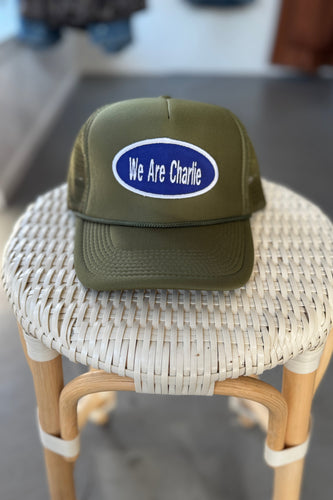 Green cap with 'We Are Charlie' logo on a woven stool