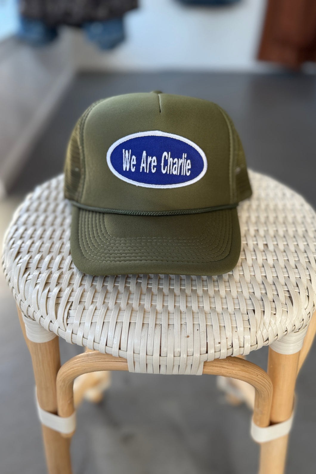 Green cap with 'We Are Charlie' logo on a woven stool