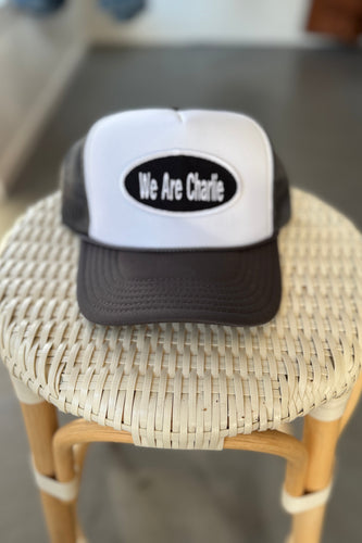 Black and white cap with 'We Are Charlie' text on a woven stool.