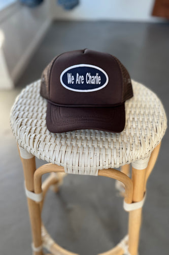 Brown cap with 'We Are Charlie' logo on a wicker stool