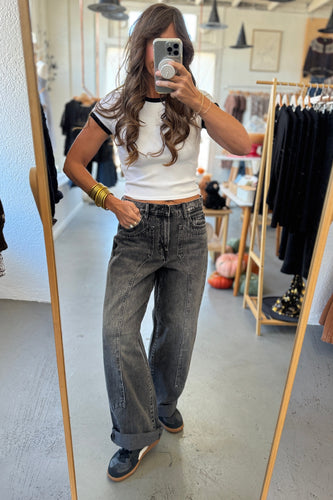 Person taking a mirror selfie wearing a white top and gray jeans in a clothing store.