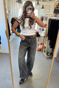 Person taking a mirror selfie wearing a white top and gray jeans in a clothing store.