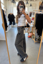 Load image into Gallery viewer, Person taking a mirror selfie wearing a white top and dark jeans in a clothing store.