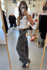 Person taking a mirror selfie wearing a white top and dark jeans in a clothing store.