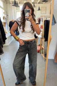Person taking a mirror selfie wearing a white crop top and dark jeans in a clothing store.