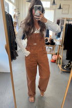 Load image into Gallery viewer, Person wearing brown overalls taking a mirror selfie in a clothing store.
