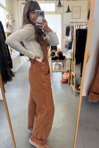 Person wearing brown overalls taking a mirror selfie in a clothing store.