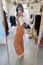 Load image into Gallery viewer, Person wearing brown overalls taking a mirror selfie in a clothing store.