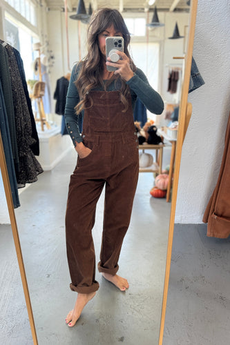 Person wearing brown overalls taking a mirror selfie in a store.