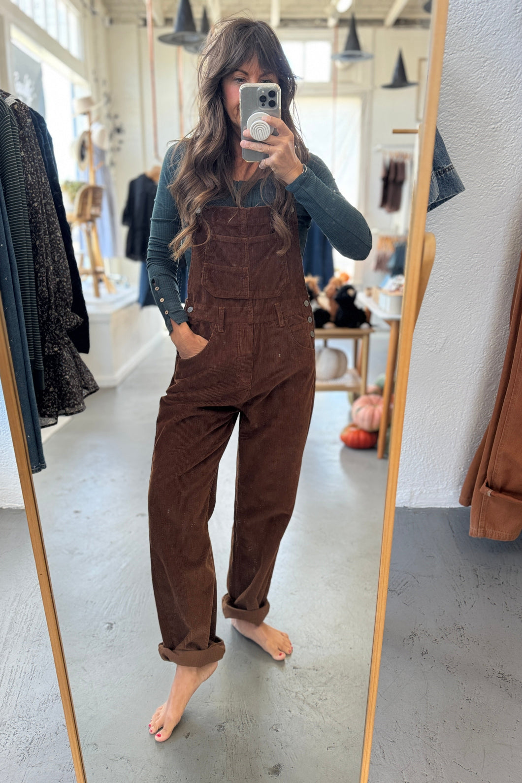 Person wearing brown overalls taking a mirror selfie in a store.
