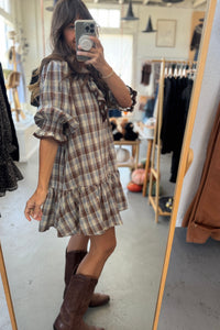 Person wearing a plaid dress and brown boots in a clothing store.