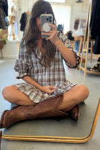 Load image into Gallery viewer, Person sitting on a mirror wearing a plaid dress and brown boots in a store setting.