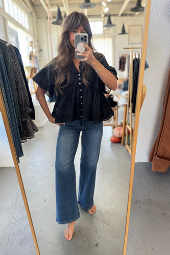 Person taking a mirror selfie wearing a black top and blue jeans in a clothing store.