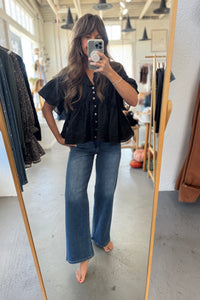 Person taking a mirror selfie wearing a black top and blue jeans in a clothing store.
