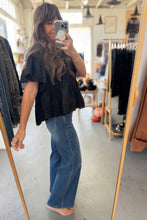Load image into Gallery viewer, Person taking a mirror selfie wearing a black top and blue jeans in a clothing store.