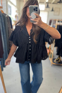 Woman taking a mirror selfie wearing a black top and blue jeans in a clothing store.