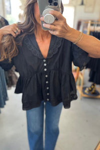 Person wearing a black blouse with white buttons and blue jeans, taking a mirror selfie.