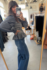Person taking a mirror selfie wearing a plaid top and blue jeans in a clothing store.
