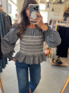 Person wearing a gray and black striped sweater with puffed sleeves in a clothing store.