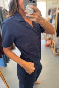 Person wearing a navy blue jumpsuit taking a mirror selfie in a clothing store.