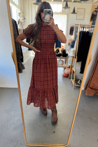 Person wearing a red plaid dress standing in front of a mirror in a store.